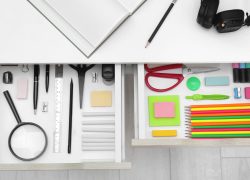 Office drawer neatly organized. Each item in its own compartment. Colourful office supplies such as paper, staples and felt tips.