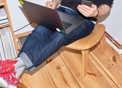 a man sitting in a room, on a chair holding a laptop with legs up on another chair