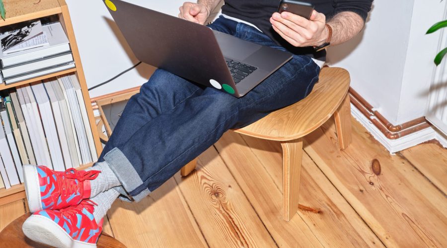 a man sitting in a room, on a chair holding a laptop with legs up on another chair