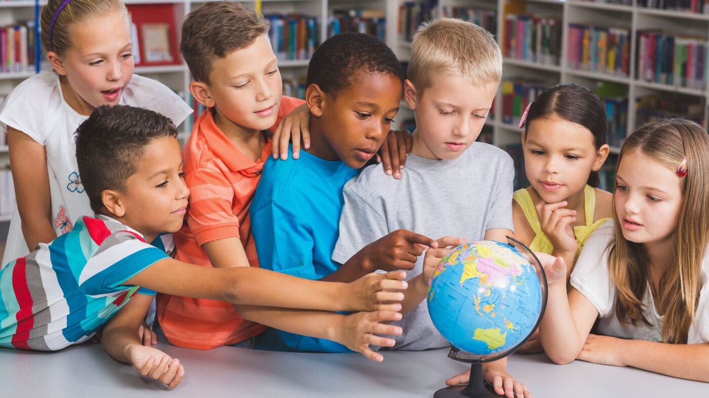 A group of children gathered around a world globe examining it to present the unity and inclusion in Erasmus+ programme