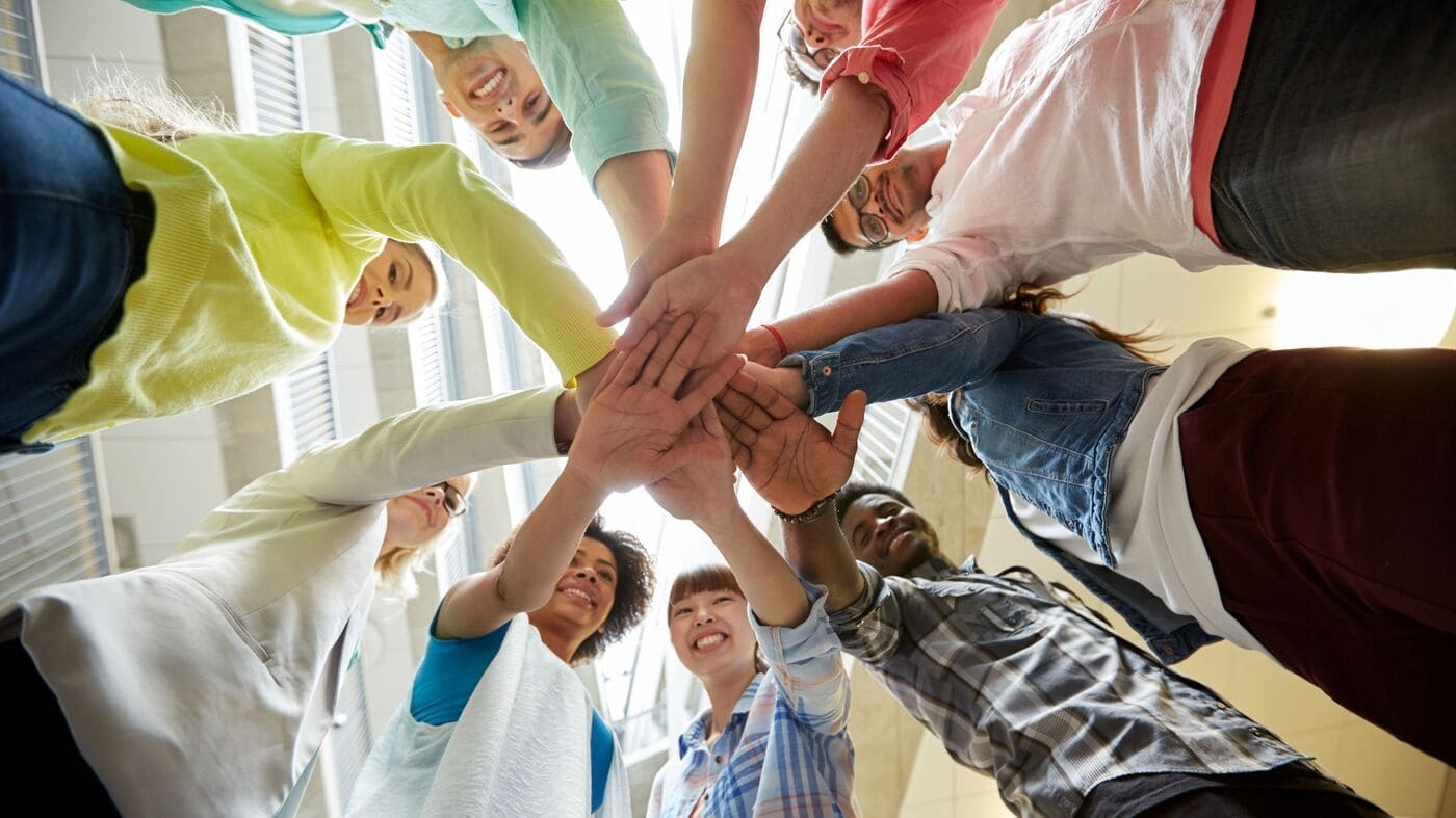 a group of young students taken from down up, uniting their hands together forming a flower like picture, smiling to show unity for inclusion in new Erasmus+ programme guide
